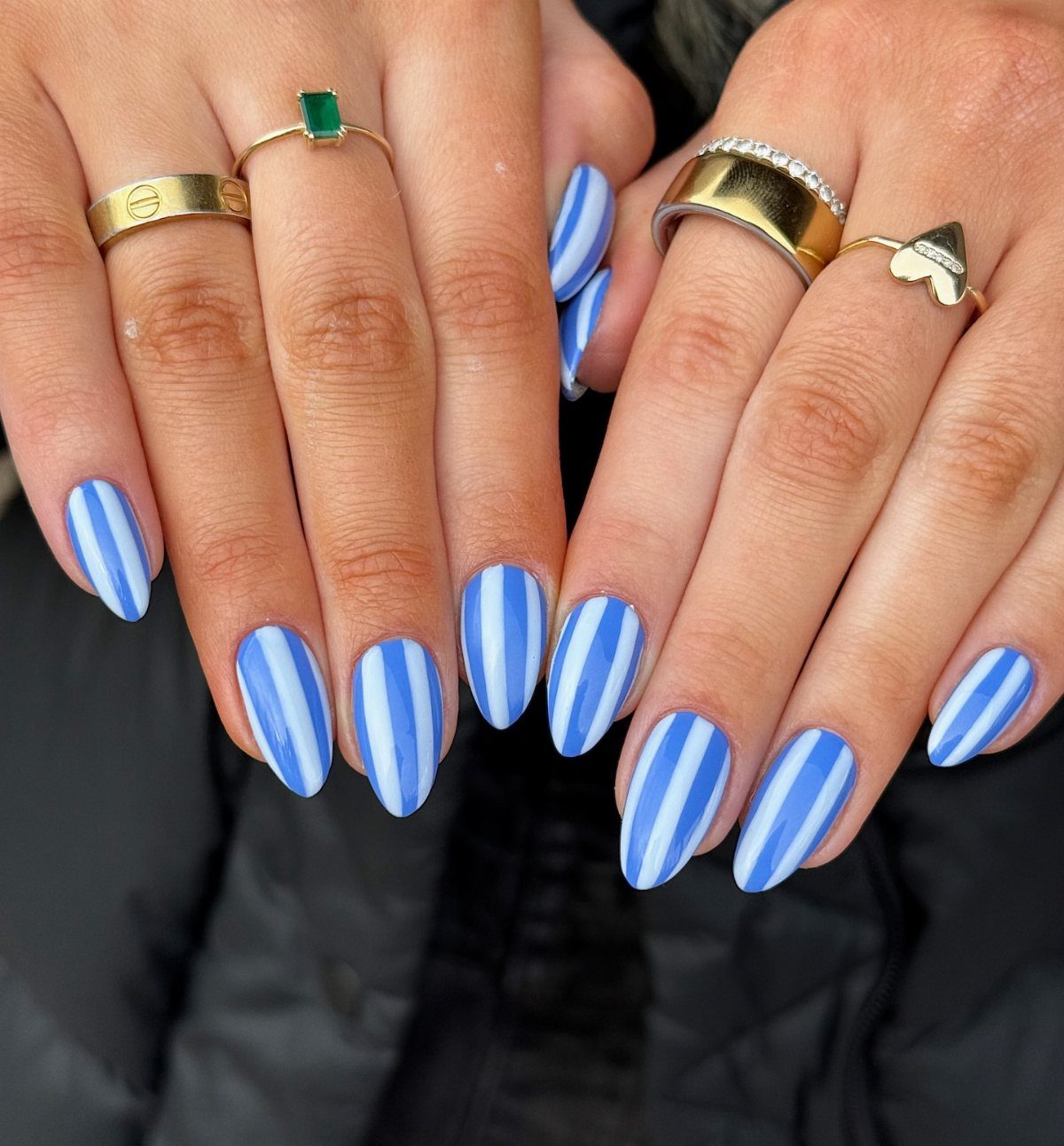 Almond-shaped nails with blue and white vertical stripes and gold rings on fingers.