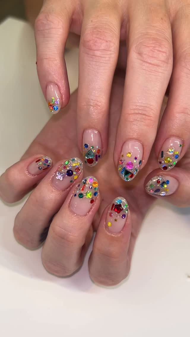 Manicured nails with colorful glitter confetti sequins on a clear base.