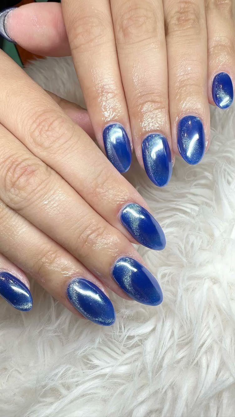 Vibrant electric blue metallic nails on hands resting on white faux fur.