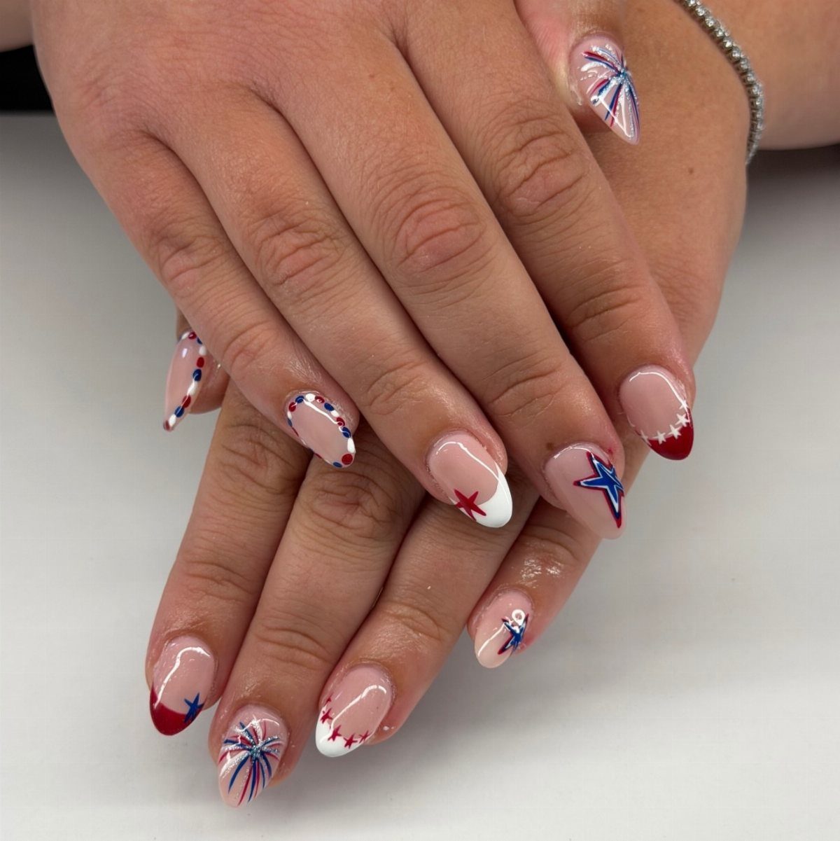 Patriotic almond nails with red, white, and blue firework and star designs.