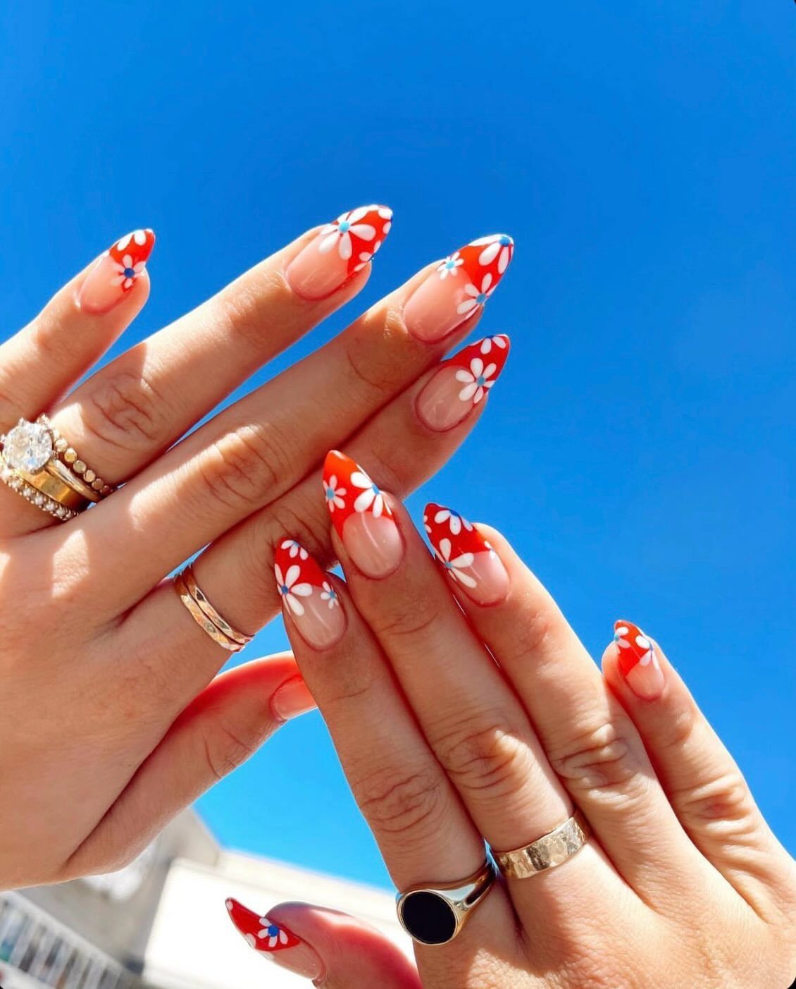 Almond nails with red tips and white floral patterns against a blue sky
