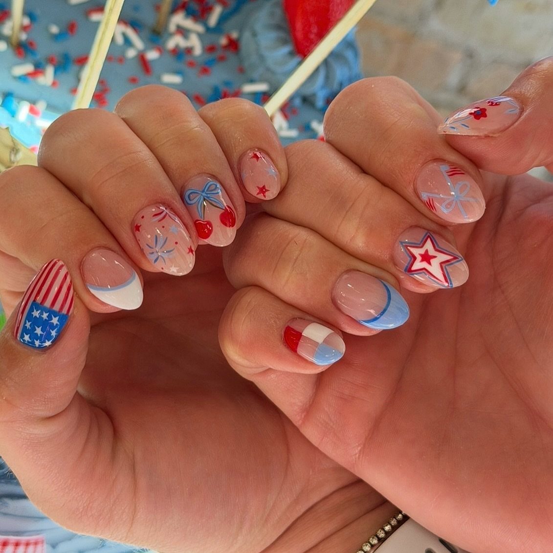 Patriotic red, white, and blue nail art with stars and stripes on hands.
