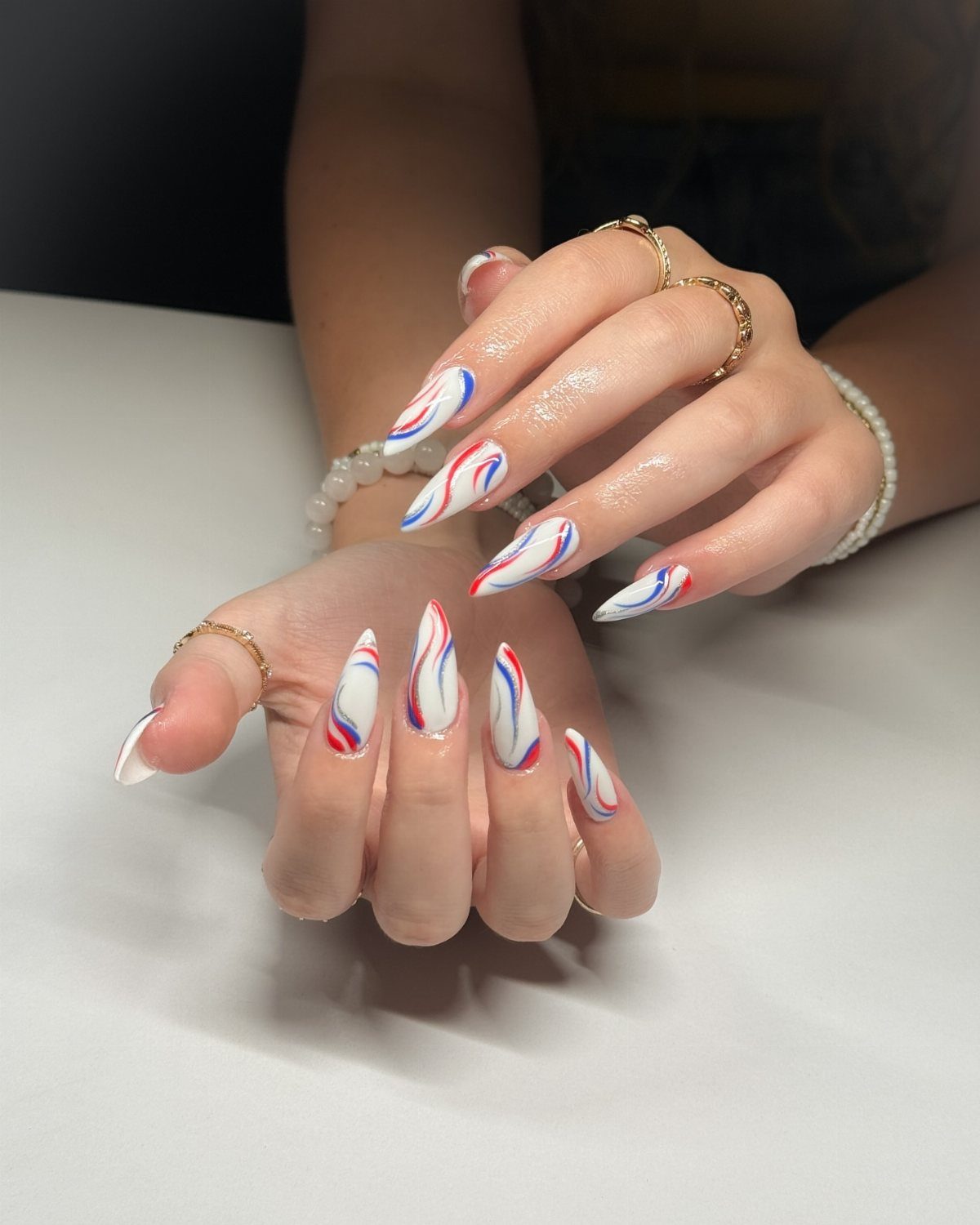 Almond-shaped nails with white base and red and blue swirling patriotic patterns.