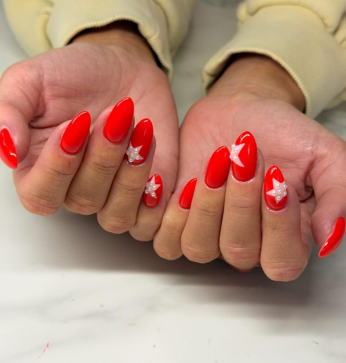Red almond-shaped nails with white star accents on a white marble background