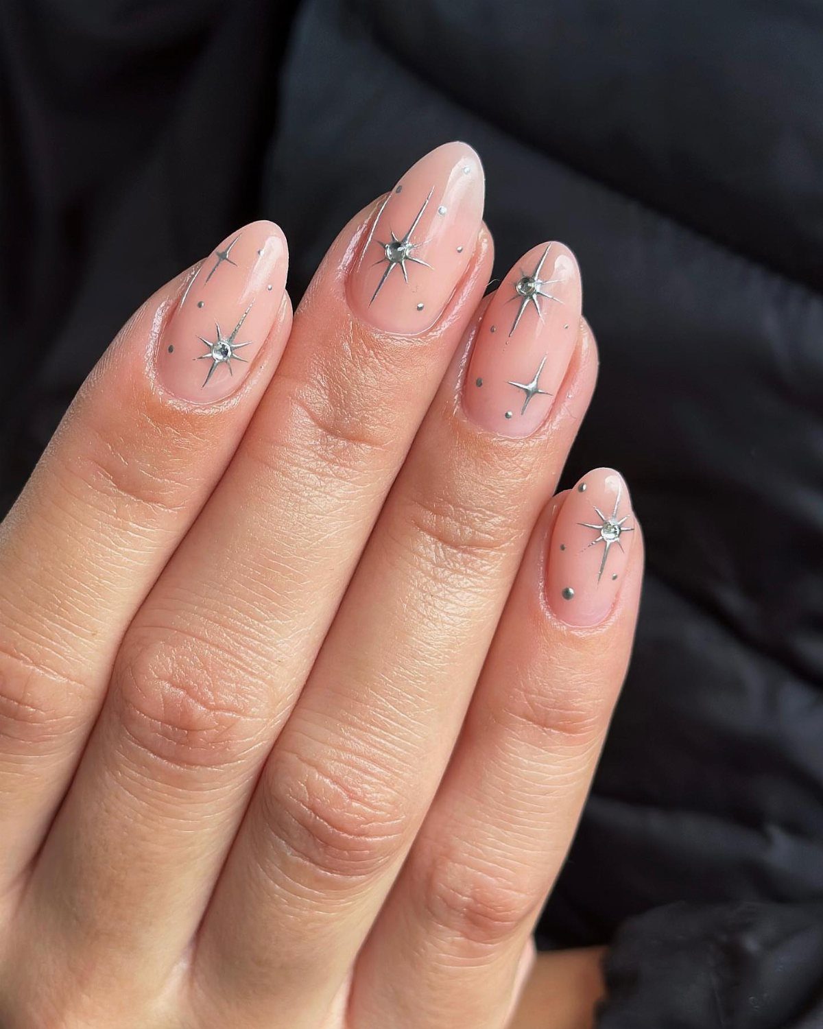 Nude almond nails decorated with minimalist shimmering silver stars and tiny dots.