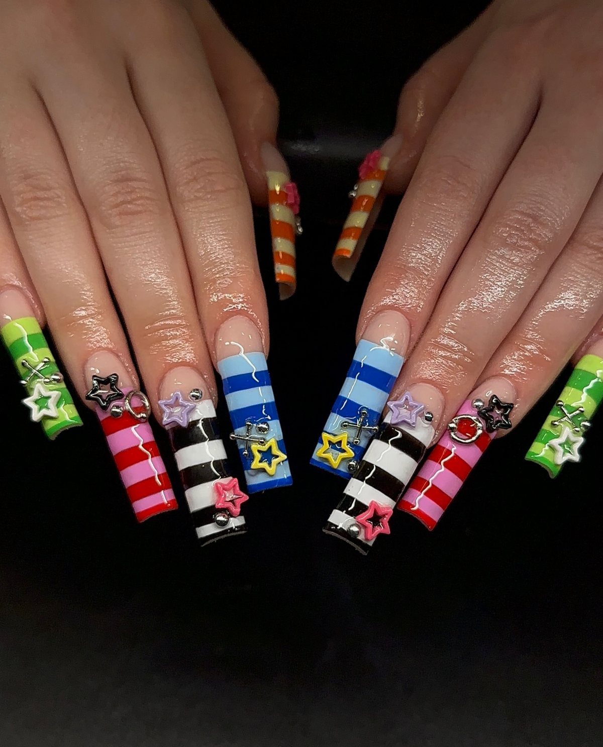 Long striped acrylic nails with colorful patterns and 3D star studs on fingers.