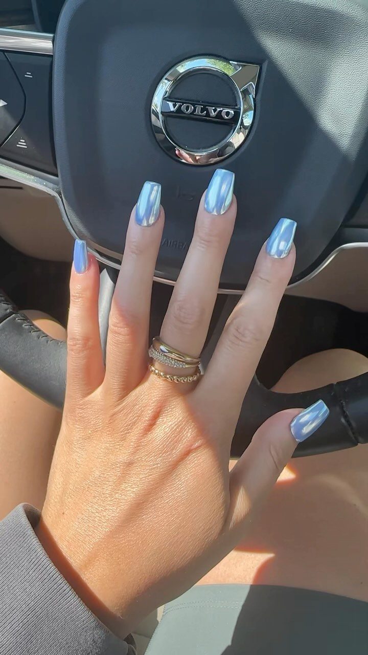 Light blue chrome nails on a hand resting on a Volvo steering wheel