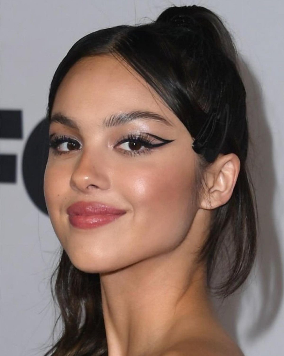 Woman with sharp black winged eyeliner and pink lipstick posing for a portrait.