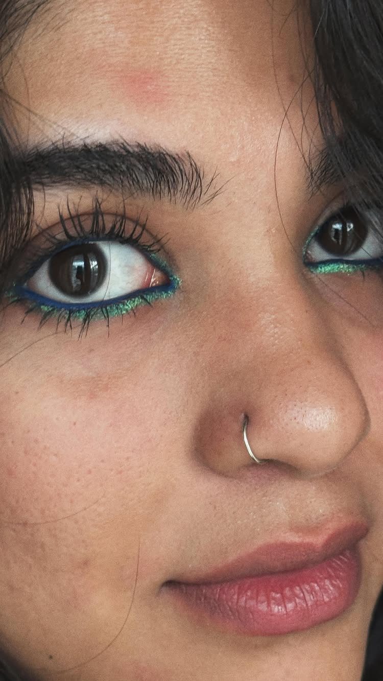 Person with blue and green eyeliner on lower lids and a nose ring.