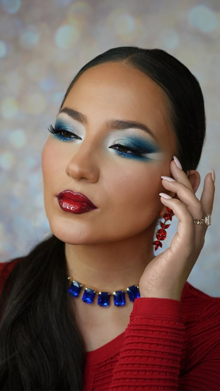 Woman wearing bold red lipstick and blue eyeshadow with a red sweater.
