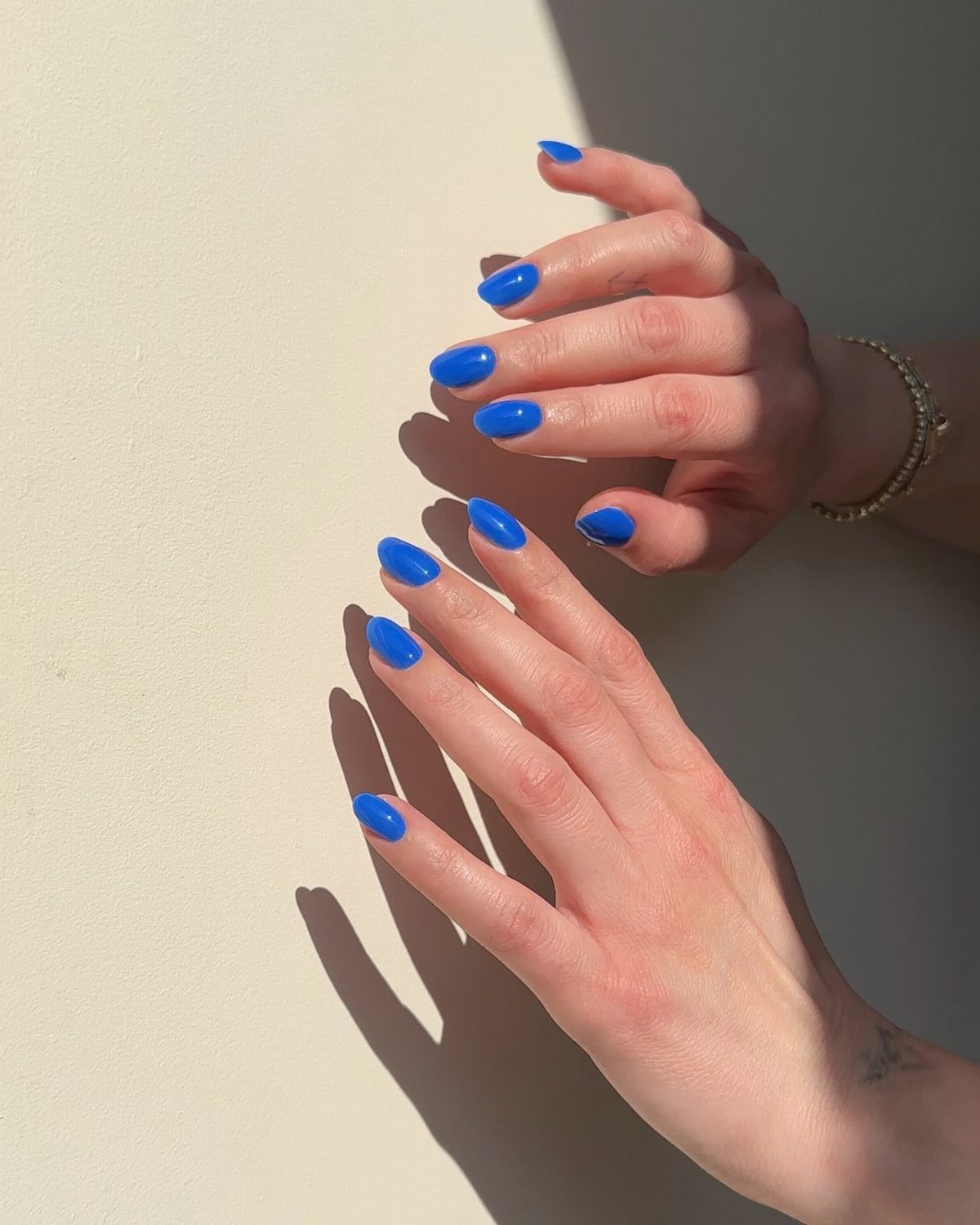 Vibrant electric-blue gel nails on two hands resting on a sunlit surface.