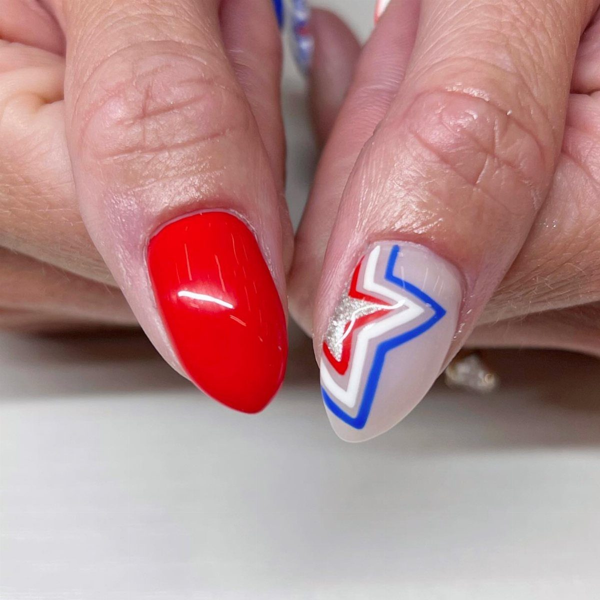 Red and blue patriotic nail art with silver glitter on a hand.