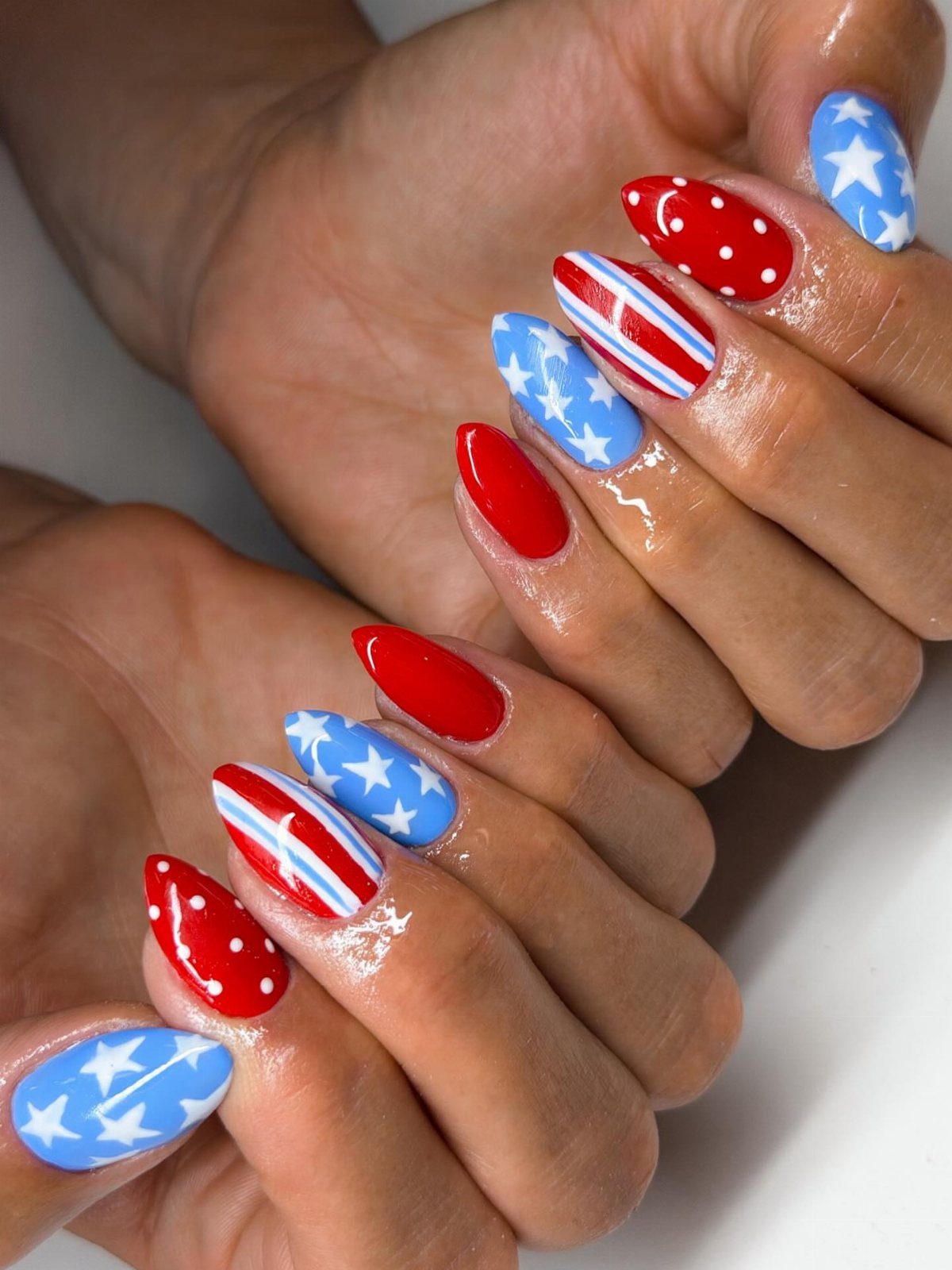 Patriotic almond nails with red polka dots, blue stars, and red white stripes.
