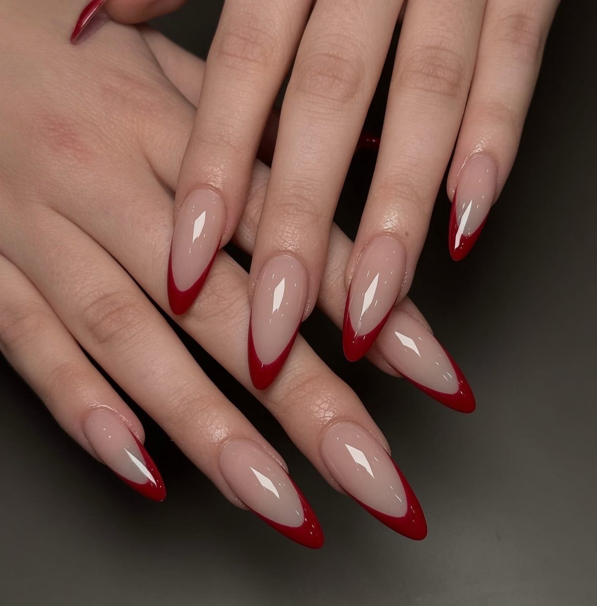 Almond-shaped nails with a nude base and bold red French tips.