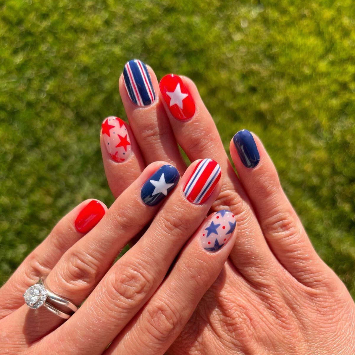 Red, white, and blue gel nails with stars and stripes motifs on grass.