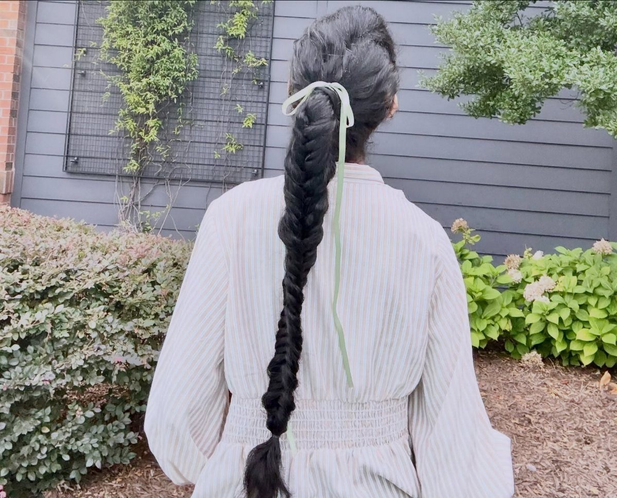 Long dark fishtail braid tied with a light green ribbon on a person.