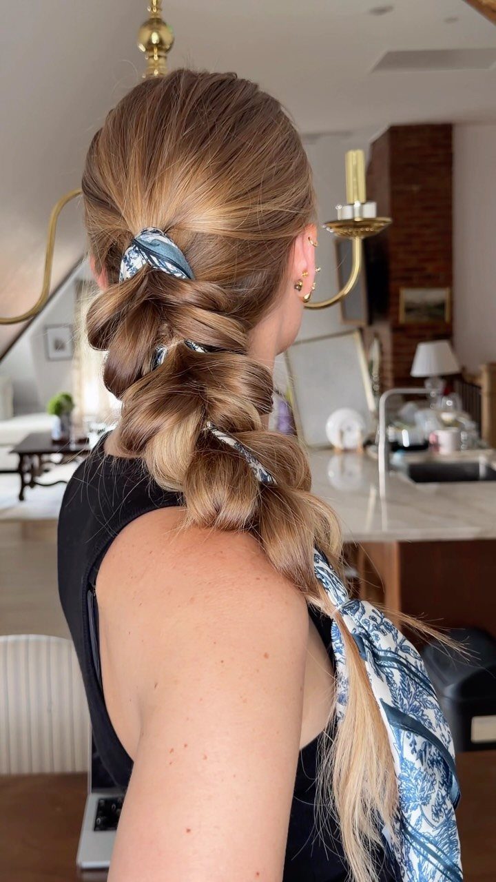 Woman's light brown hair styled in a loose braid with a blue patterned scarf.