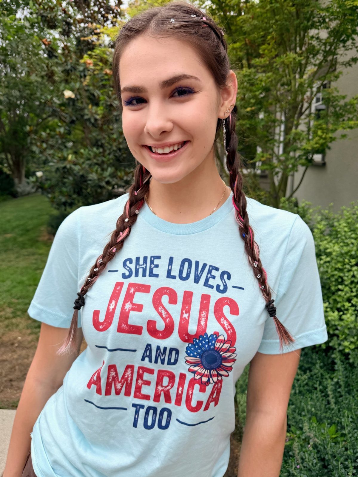 Young woman with red, white, and blue braided hair wearing a patriotic t-shirt.