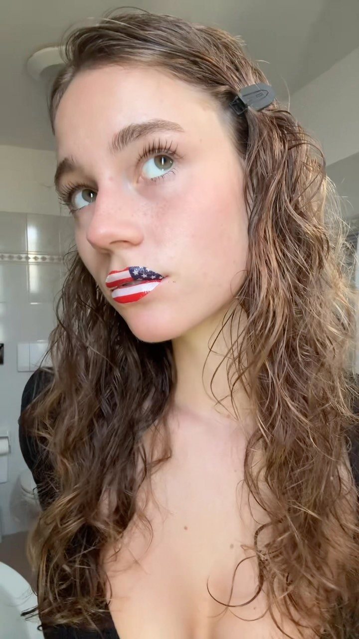 Woman with wavy brown hair wearing American flag lipstick in a bathroom
