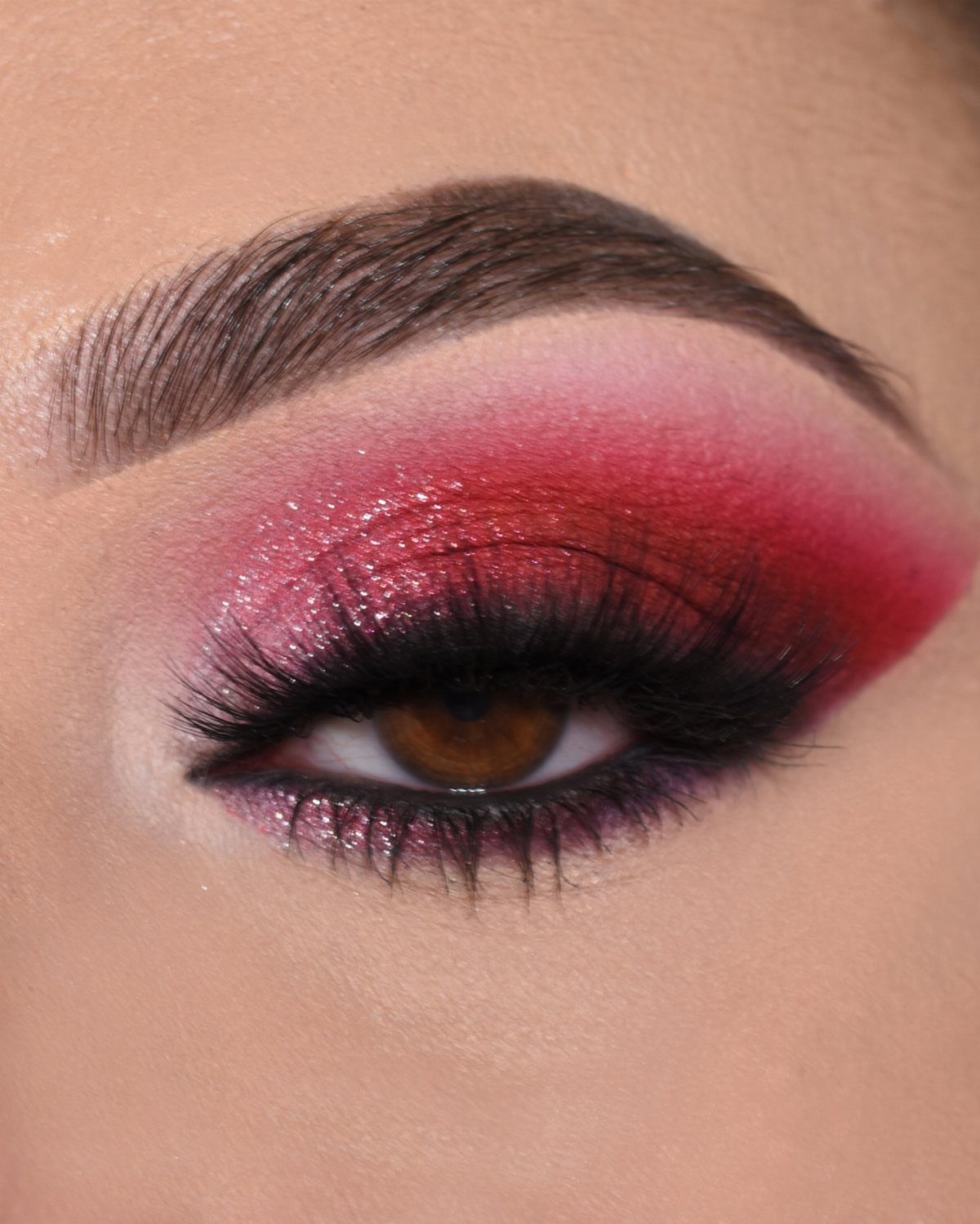 Eye with bold red and pink shimmering eyeshadow and long black lashes.