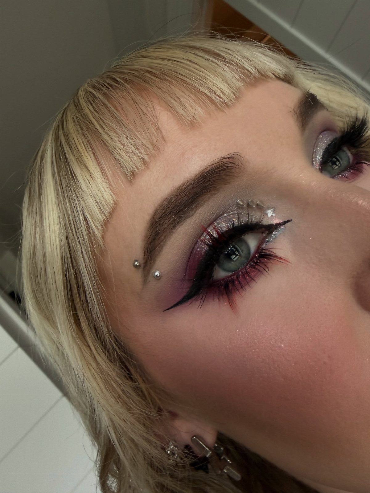 Eye makeup with black winged liner, red lower lid, and silver glitter accents.