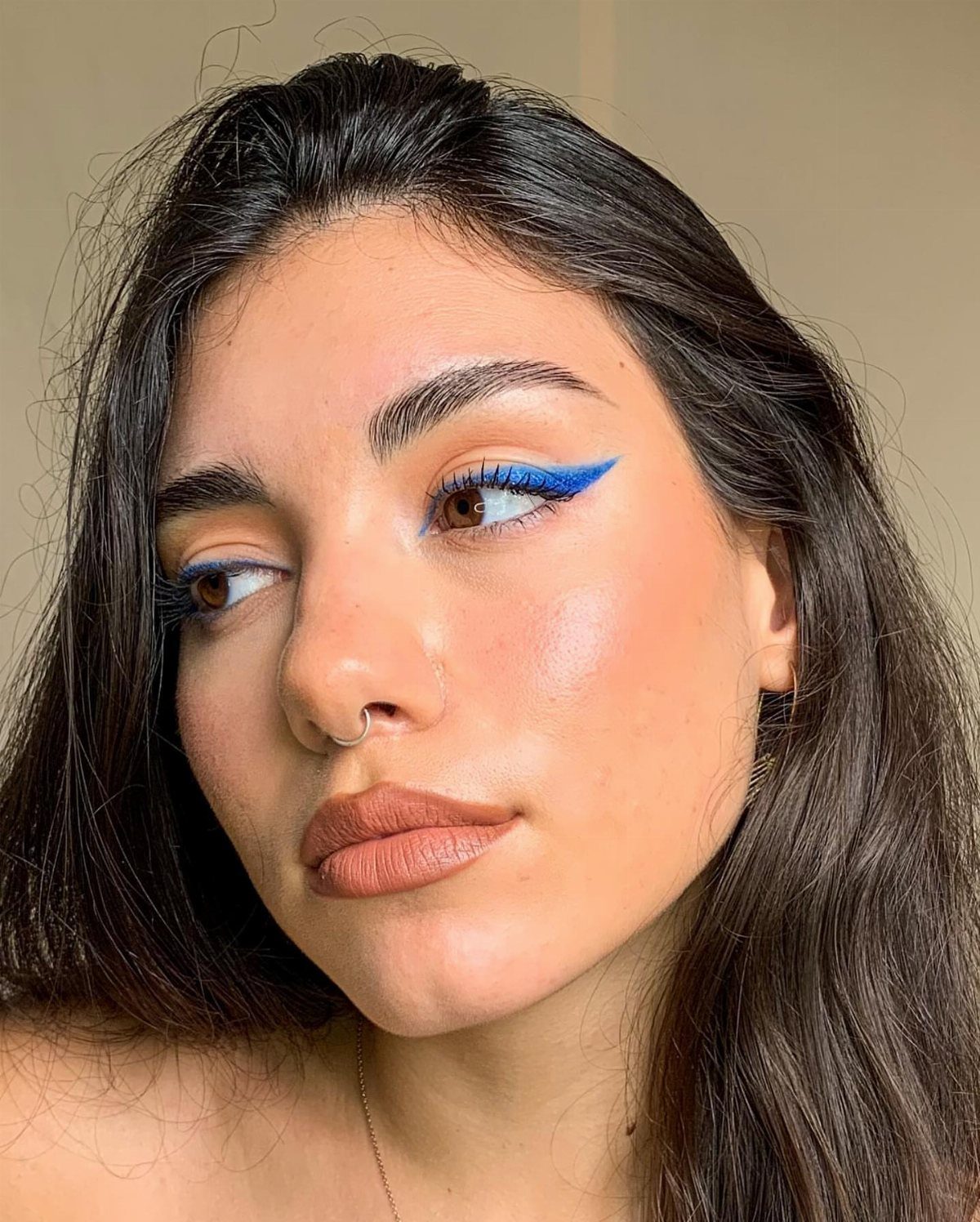 Woman with bright blue winged eyeliner and matte brown lipstick posing for portrait