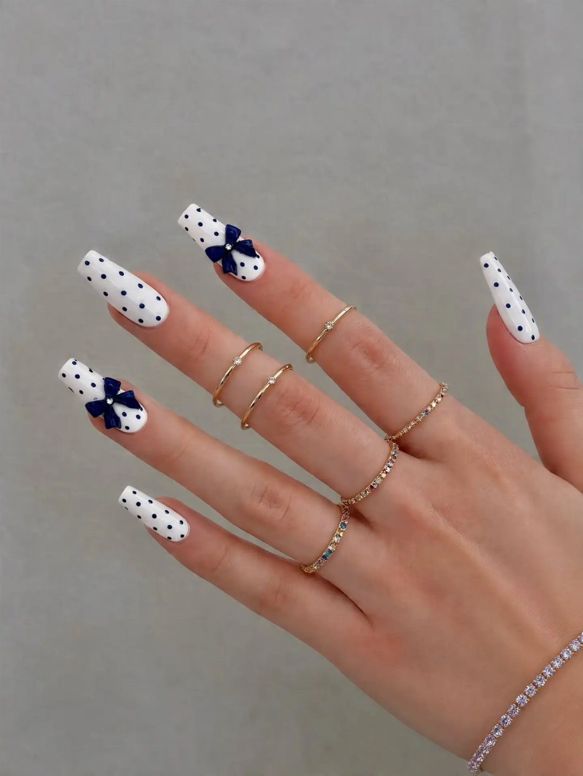White coffin nails with blue polka dots and bows on a hand.