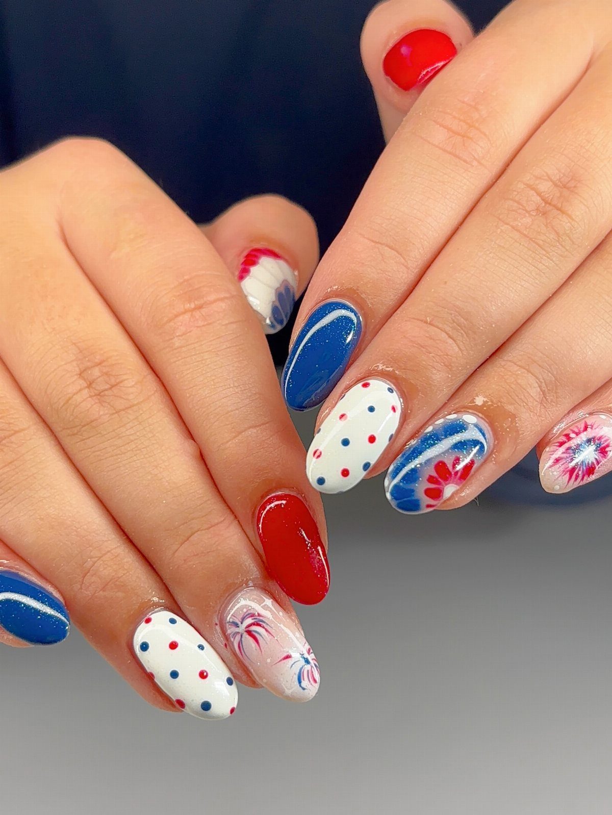 Patriotic red, white, and blue nail art featuring polka dots and fireworks designs.