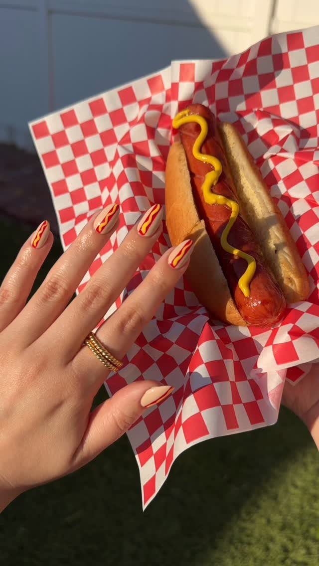 Hand with hot dog nail art holding a real hot dog with mustard.