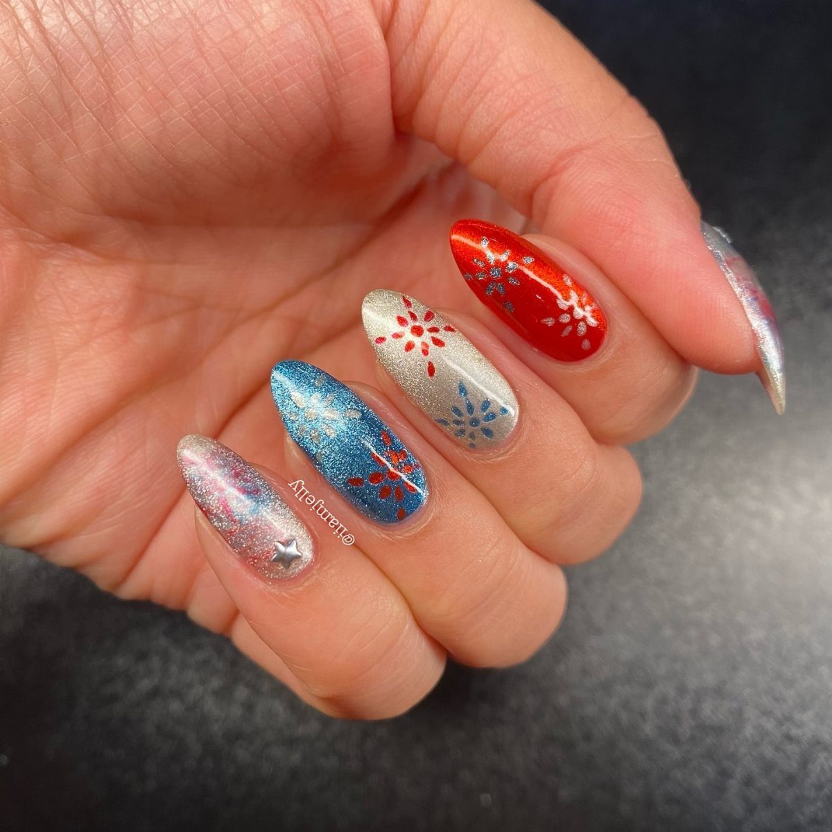Patriotic red, white, and blue glitter nails with star patterns on a hand.