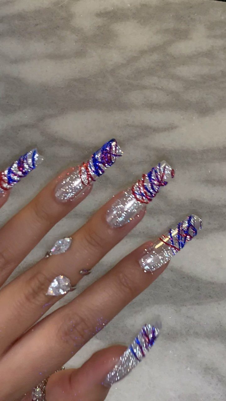 Long coffin nails with silver glitter and red, white, and blue 3D swirls.