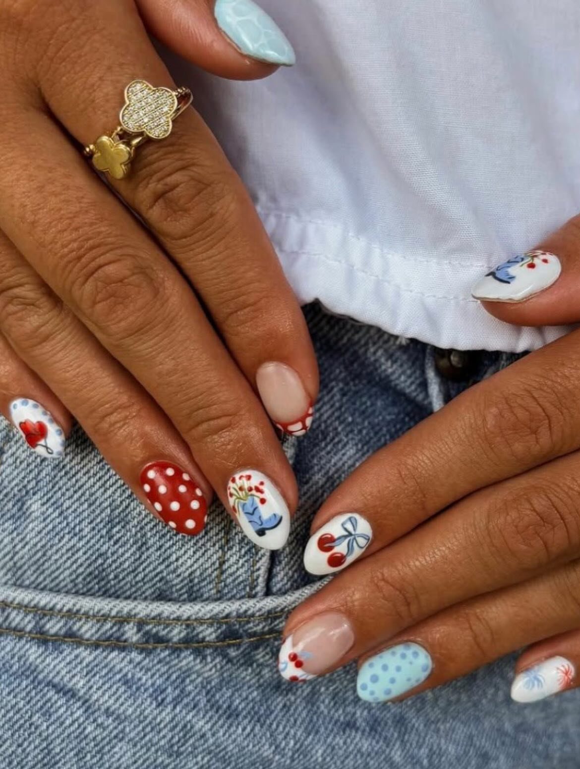 Manicured nails with red, white, and blue patterns resting on blue denim jeans.