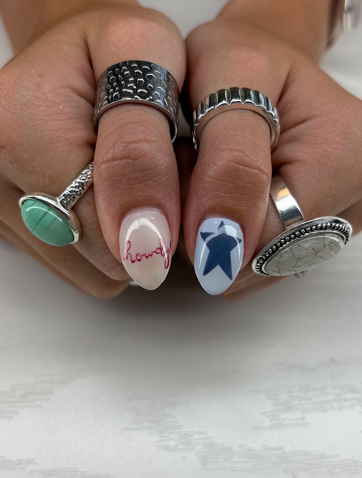 Manicured nails with red text and a blue star, adorned with silver rings.