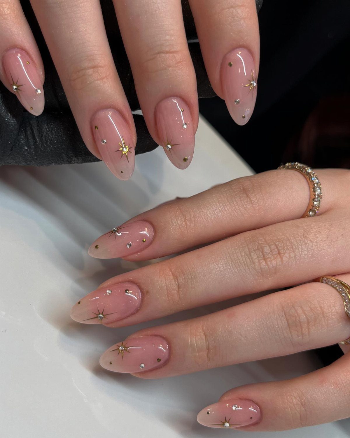 Nude almond-shaped nails decorated with small gold stars and tiny white dots.
