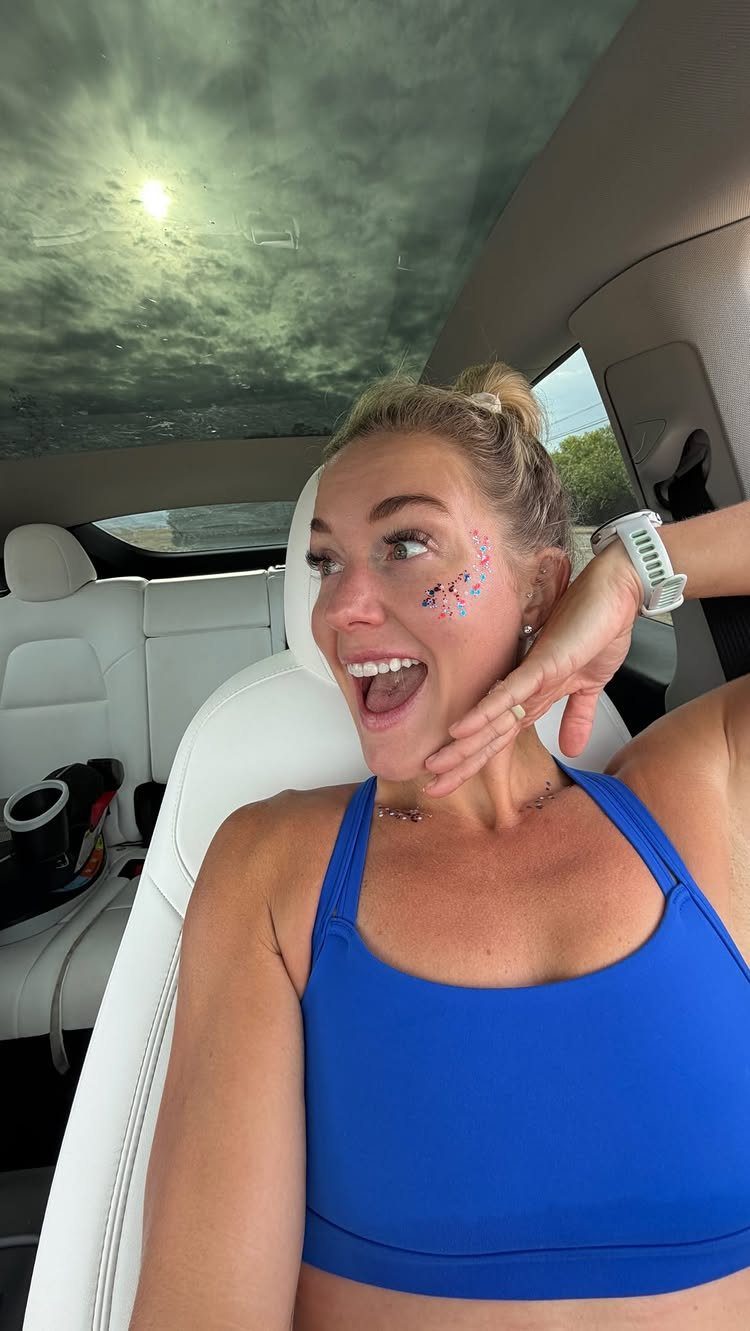 Woman in blue sports bra with patriotic glitter on her cheek inside a car