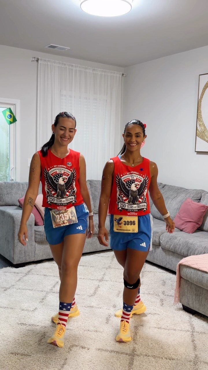 Two women wearing red white and blue running outfits with race bibs indoors.