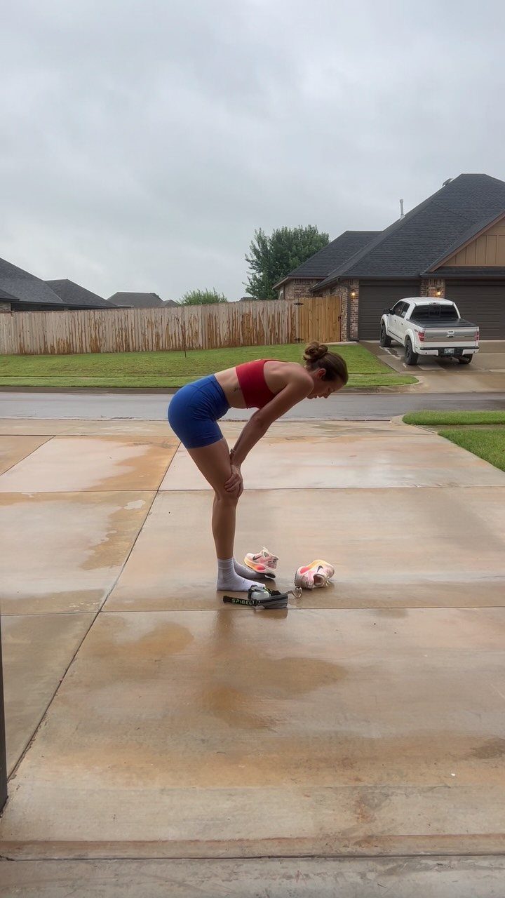 Woman in red and blue athletic wear tying shoes on a concrete driveway