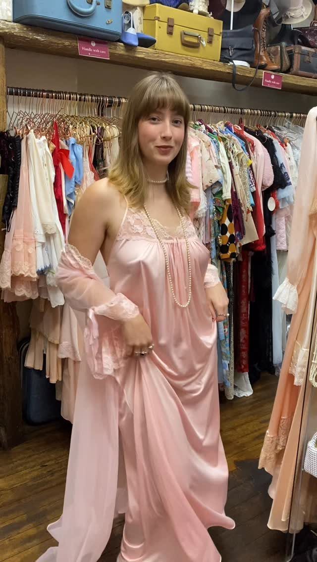 Woman wearing a pink satin slip dress and pearls in a vintage shop