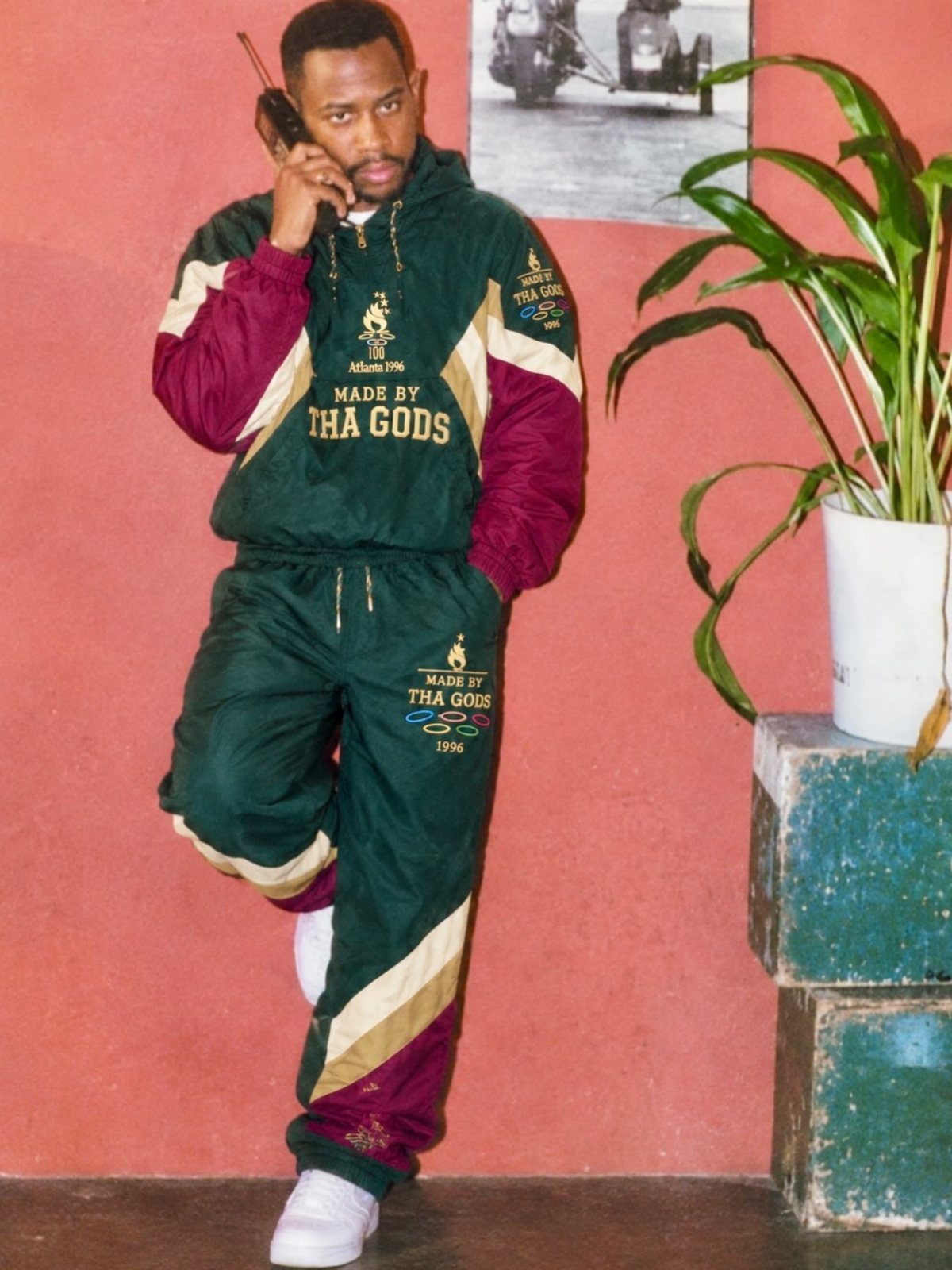 Man in a green and burgundy color-blocked tracksuit posing against a pink wall.