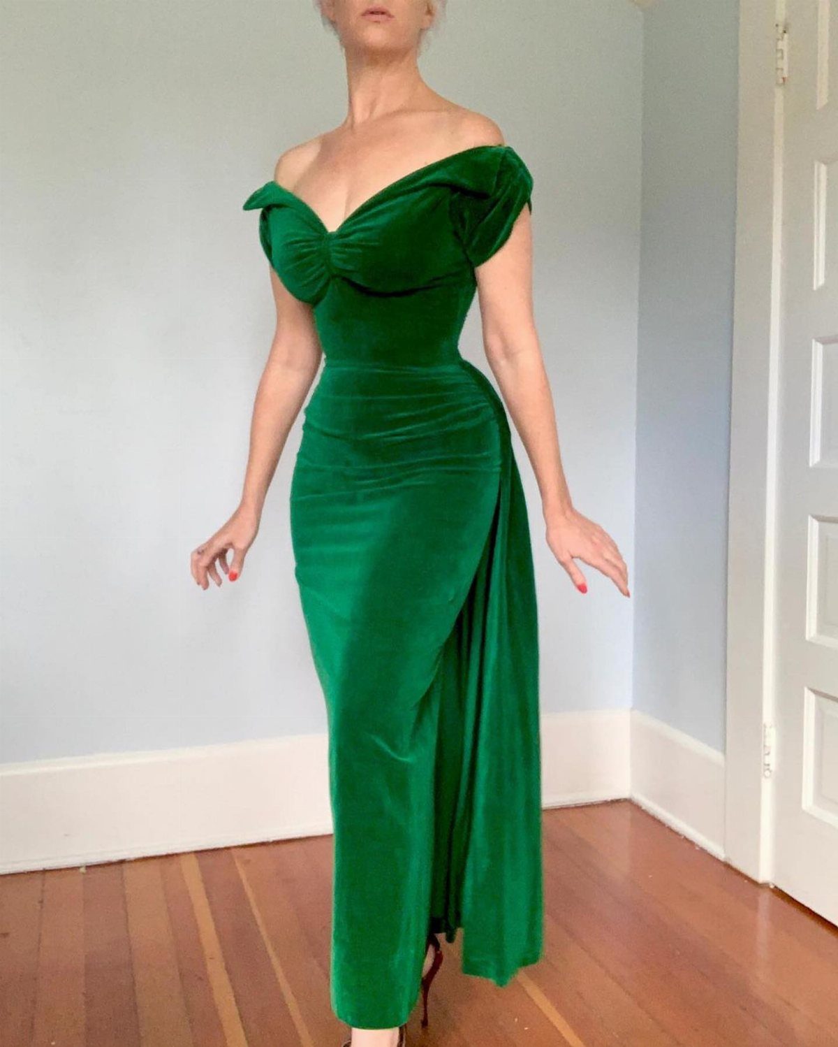 Person wearing a long emerald green velvet off-the-shoulder gown in a bright room.
