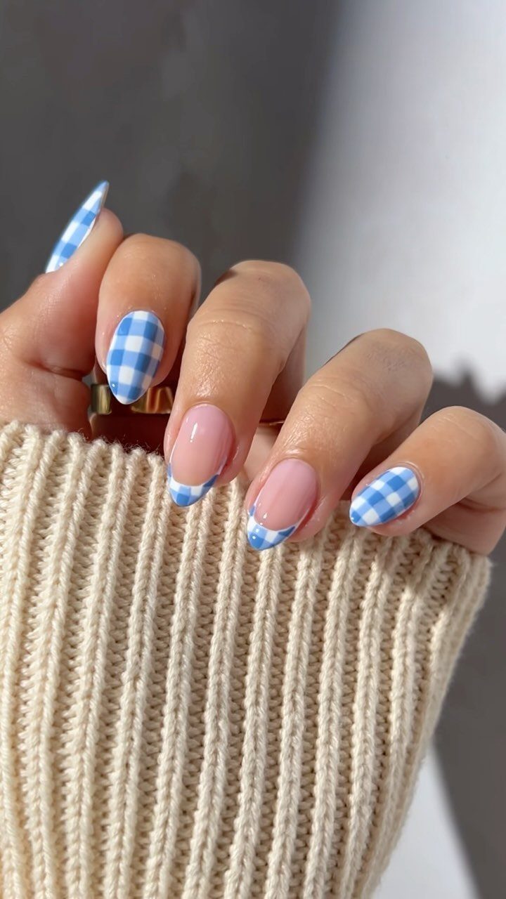 Acrylic nails with blue and white checkered patterns on a hand wearing beige sweater