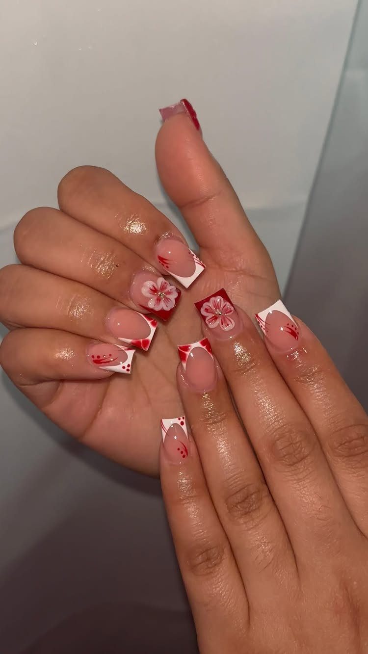 Long acrylic nails with red floral art and white tips on a hand.