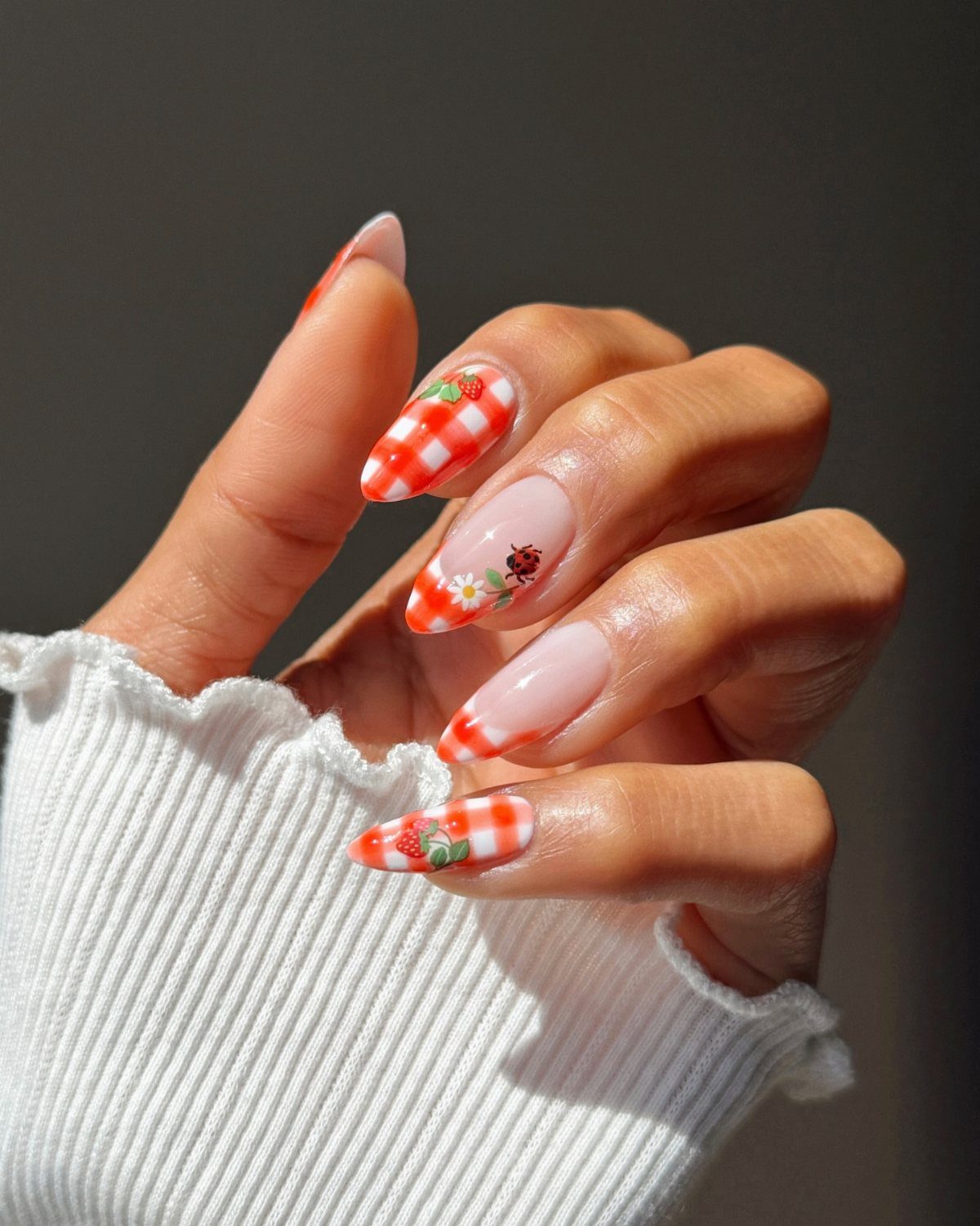 Almond acrylic nails featuring red and white gingham patterns with strawberry and ladybug accents.