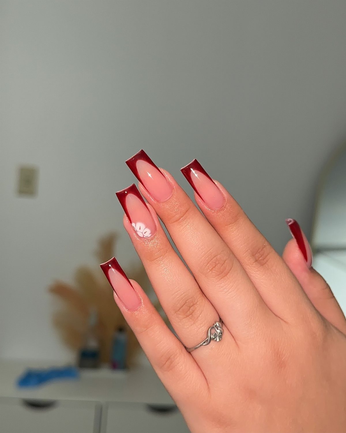 Long coffin acrylic nails with red French tips and a white 3D flower.