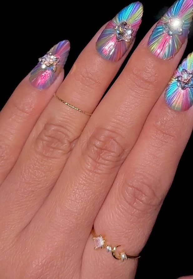 Iridescent starburst acrylic nails with sparkling rhinestone stars and thin gold rings.