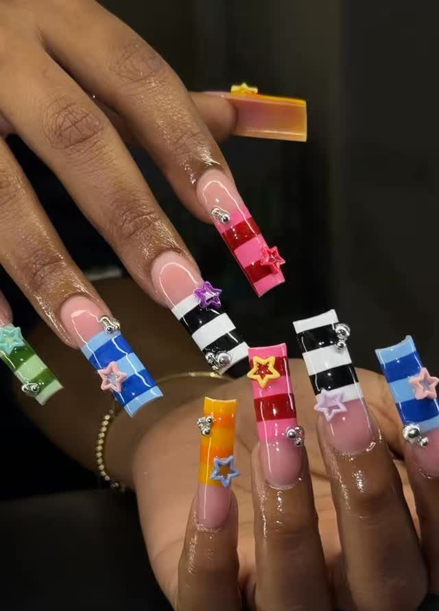 Long acrylic nails with colorful horizontal stripes, silver studs, and star charms.