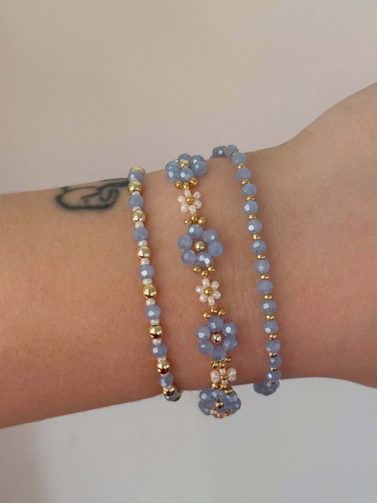 Three light blue and gold beaded bracelets worn on a person's wrist.