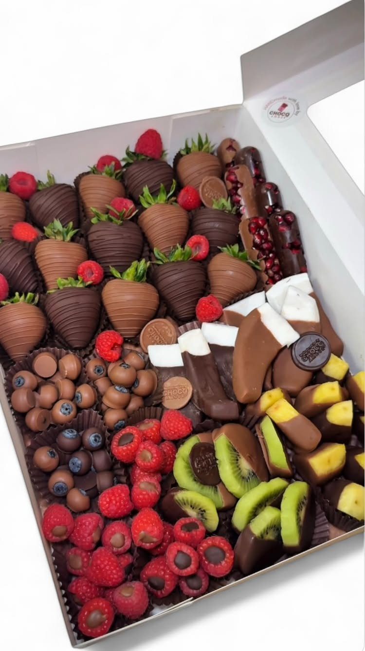 Chocolate covered strawberries and assorted fruits arranged in a white gift box.