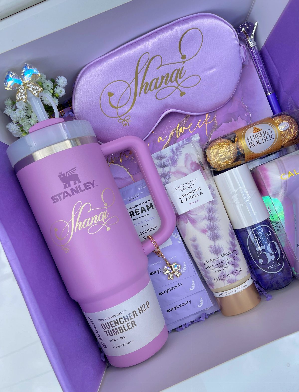 Purple gift box with Stanley tumbler, sleep mask, lotions, and chocolate on purple shredding.