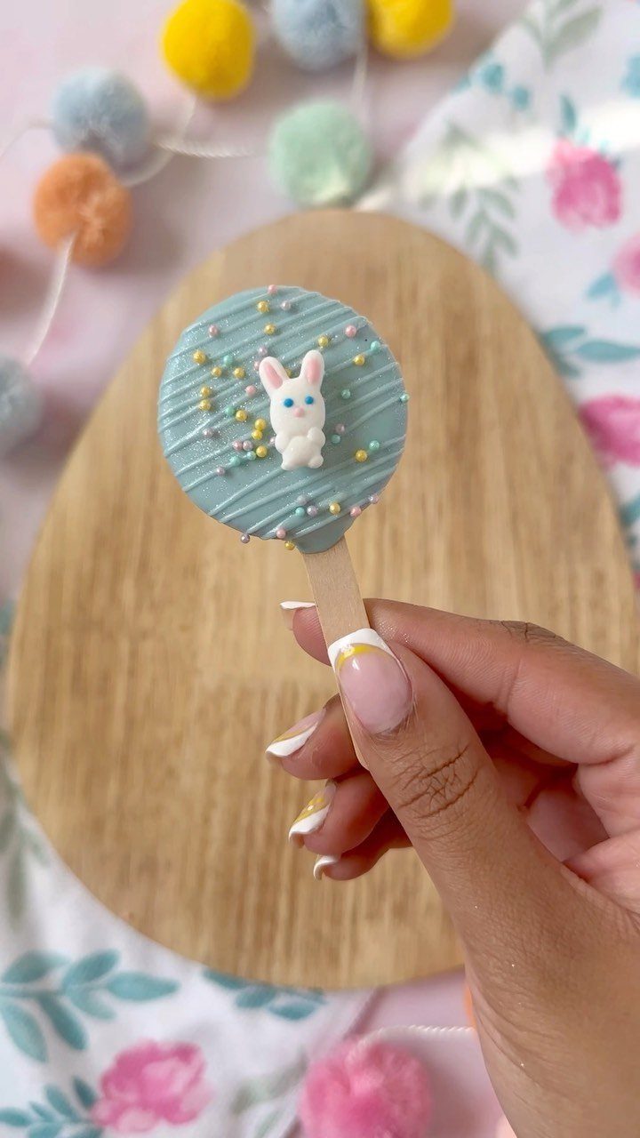 Blue chocolate cake pop with a white bunny figure held by a hand.